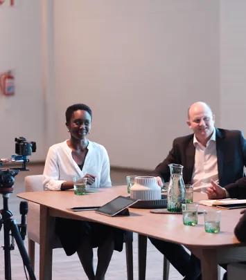 Two professionals seated at a meeting table with filming equipment